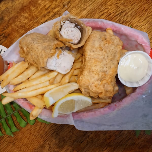 Fish and chips with lemon wedges and tartar sauce in a red basket on a wooden table.