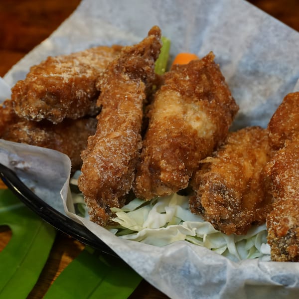 Crispy fried chicken wings with shredded cabbage, celery, and carrots in a basket at Johnny's Wingz N Tingz.