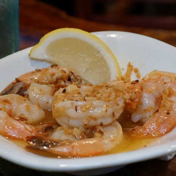 Garlic butter shrimp with a lemon wedge in a white bowl at Johnny's Wingz N Tingz.