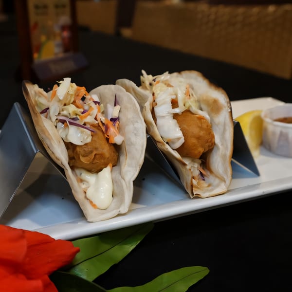 Two fish tacos with fried fish, slaw, and white sauce, served with a lemon wedge.