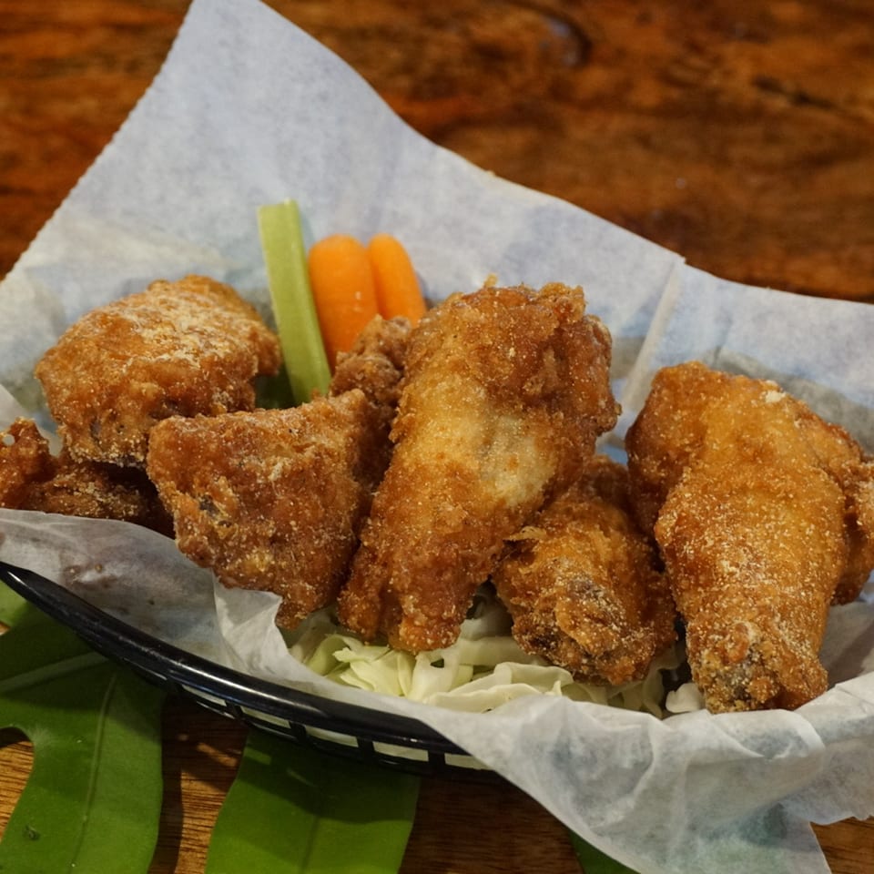 Crispy fried chicken wings with celery and carrot sticks in a basket lined with paper.