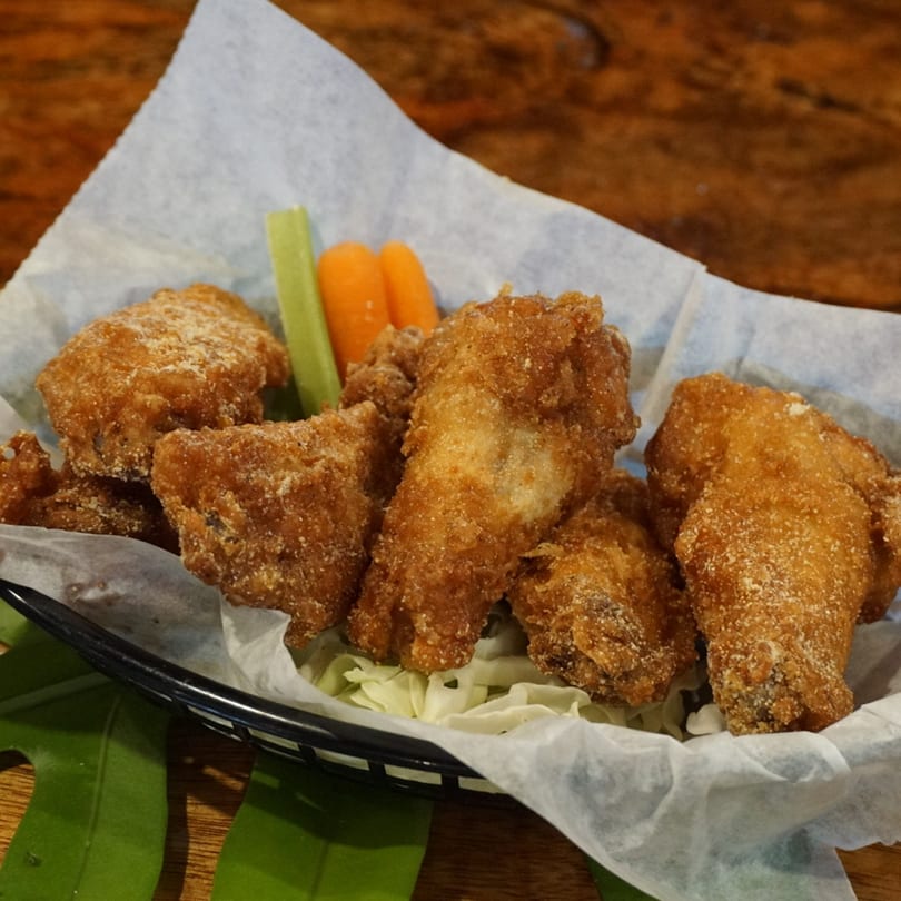 Crispy fried chicken wings with celery and carrot sticks in a basket lined with paper.