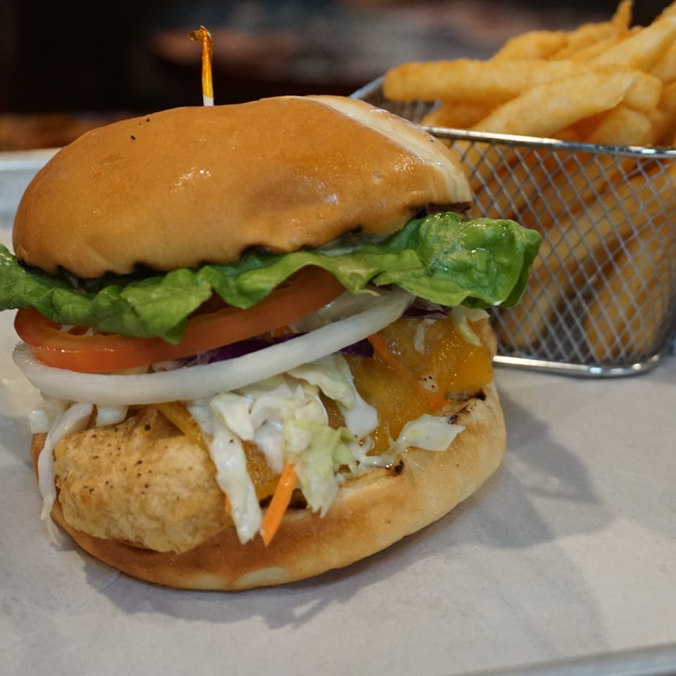 A crispy chicken sandwich with lettuce, tomato, onion, and coleslaw, served with a side of fries.