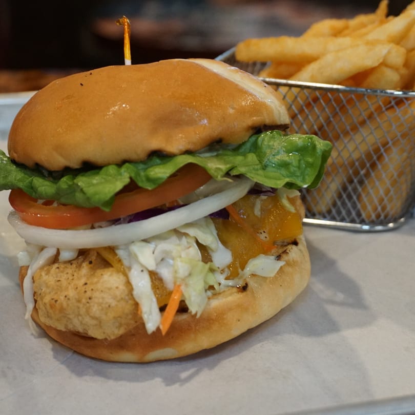 A crispy chicken sandwich with lettuce, tomato, onion, and coleslaw, served with a side of fries.