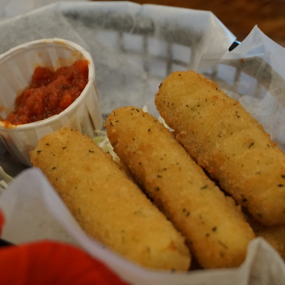 Golden-brown mozzarella sticks with herbs in a basket with a side of marinara sauce.