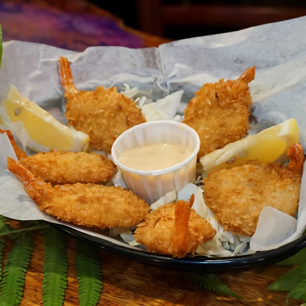 A basket of golden-brown coconut shrimp with lemon wedges and a side of dipping sauce.