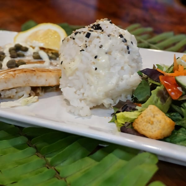 Grilled fish with capers, white rice topped with sesame seeds, and a side salad with croutons.