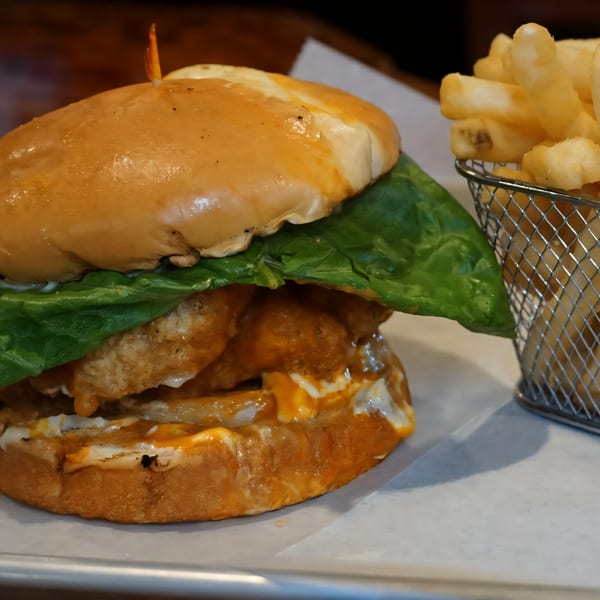 A buffalo chicken sandwich with lettuce and sauce, served with a side of french fries.