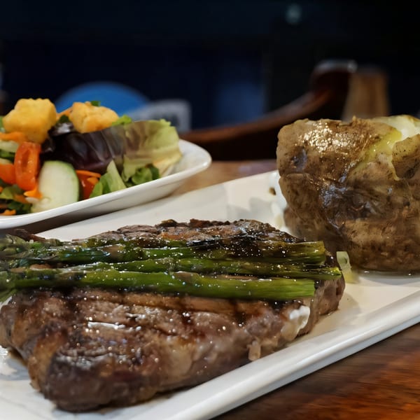 Grilled steak with asparagus, a baked potato, and a side salad on a white plate.